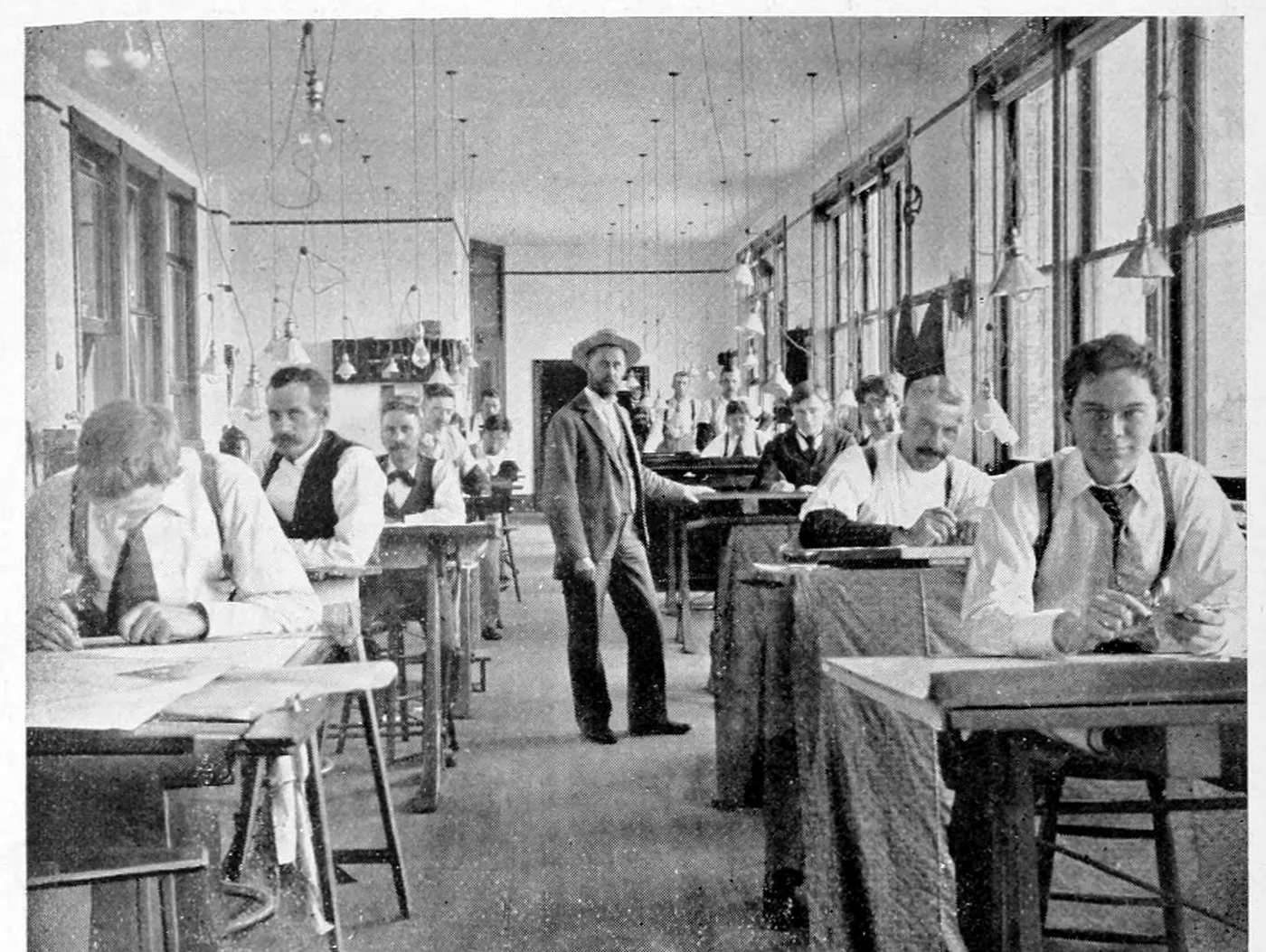Draughtsmen at their tables in the long drafting room of an iron works